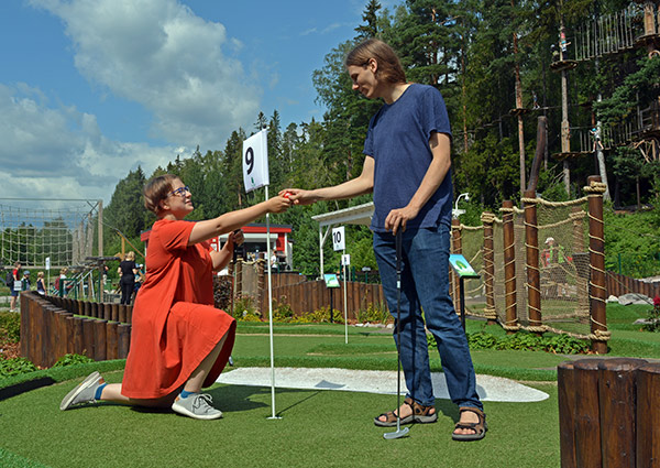 Nuori mies ja nainen seikkailugolf Huipussa. Nainen on polviseisonnassa ja ojentaa miehelle pallon.